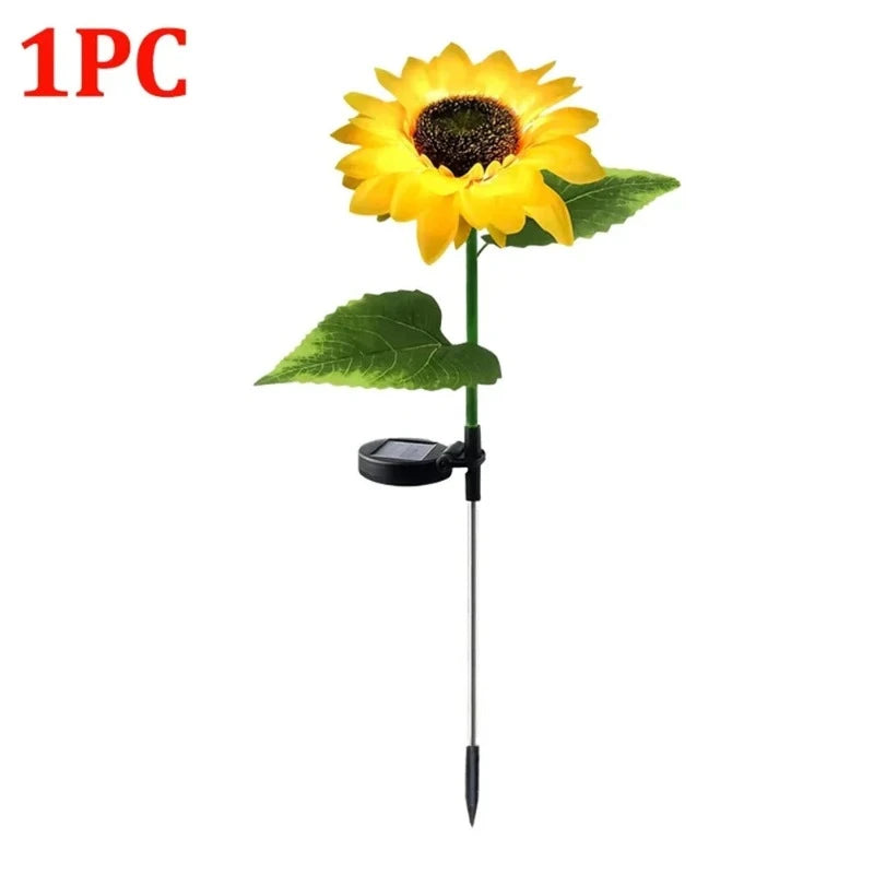 A single artificial sunflower with bright yellow petals and a dark brown center is shown on a green stem with two green leaves. A small black solar panel is attached to the stem near the base, which ends in a pointed stake. "1PC" is visible in the upper left corner against a white background.