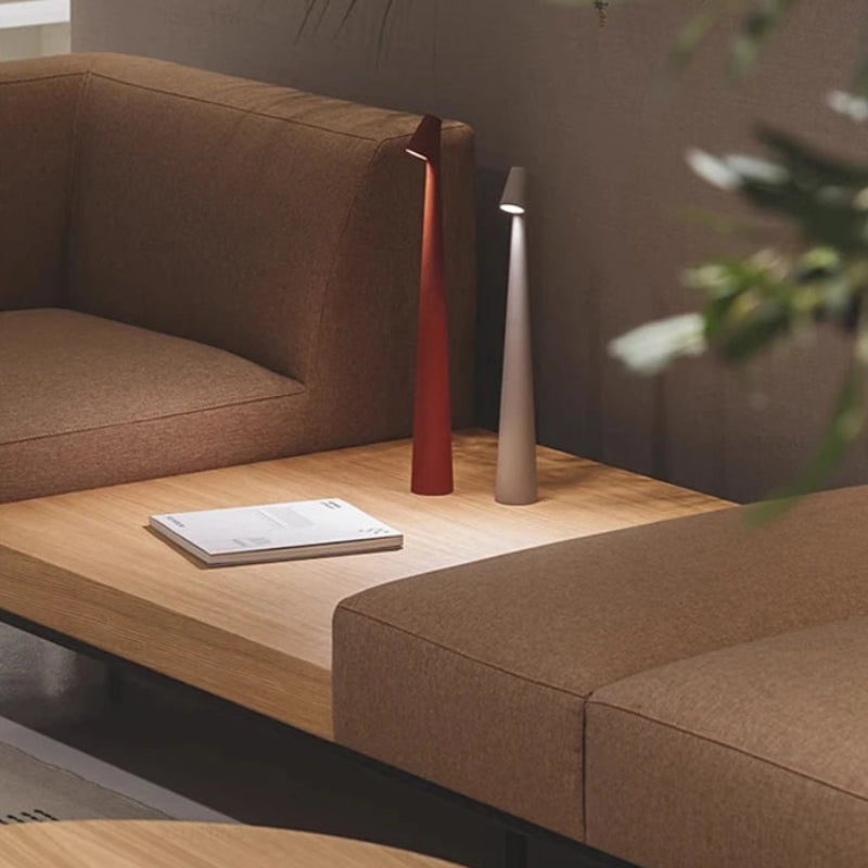 Two minimalist cone-shaped lamps, red and white, on a wooden coffee table between couches.