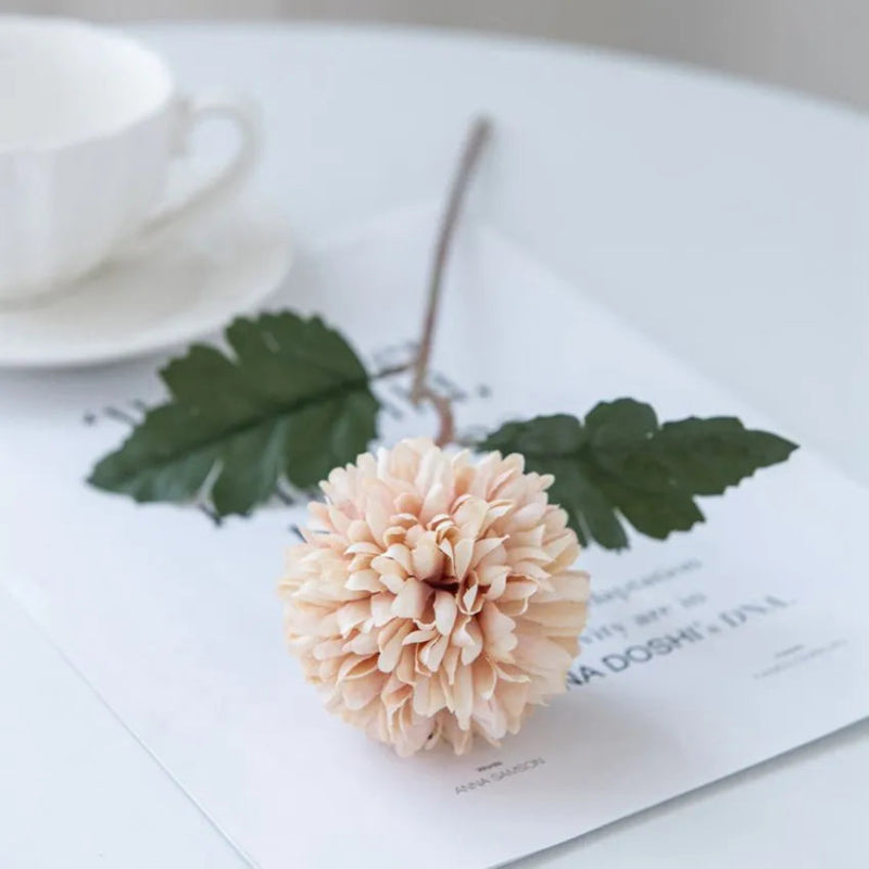 A single light pink chrysanthemum flower on a white table with a cup.