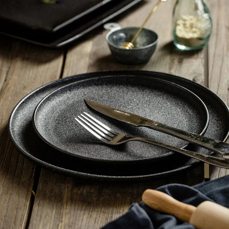 A stack of two speckled black plates with a knife and fork on a rustic wooden table.