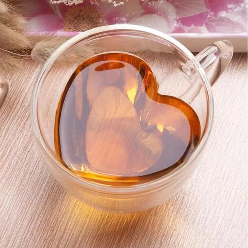 A close-up shows a clear glass teacup with a heart-shaped inner wall, filled with amber-colored tea.