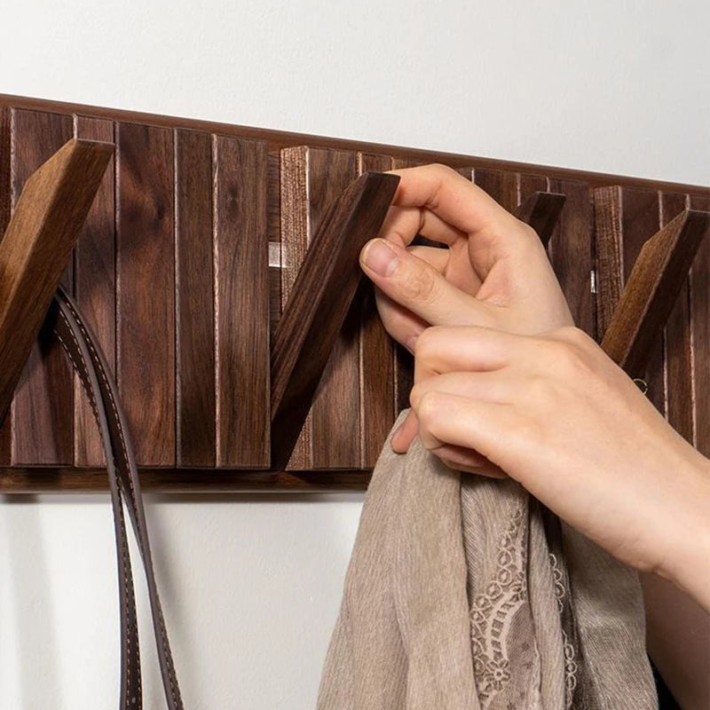 Hand hanging a beige scarf on a wooden rack against a white background