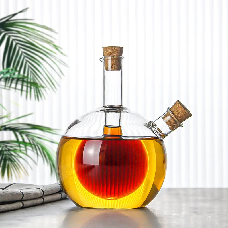 Glass decanter with two liquids, one red and one yellow, on a light surface with a plant in the background.
