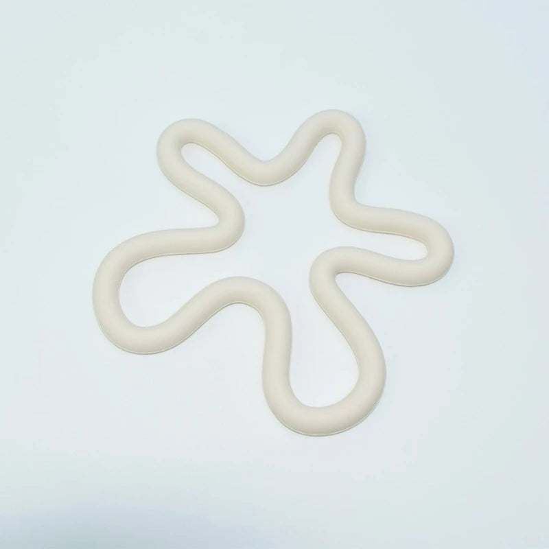 A cream-colored, wavy, abstract-shaped silicone trivet resembling a flower or splatter, placed on a white background.