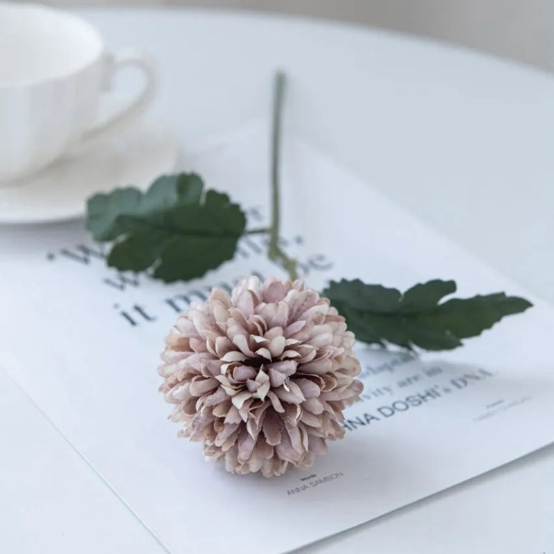 A single light purple chrysanthemum flower on a white table with a cup.