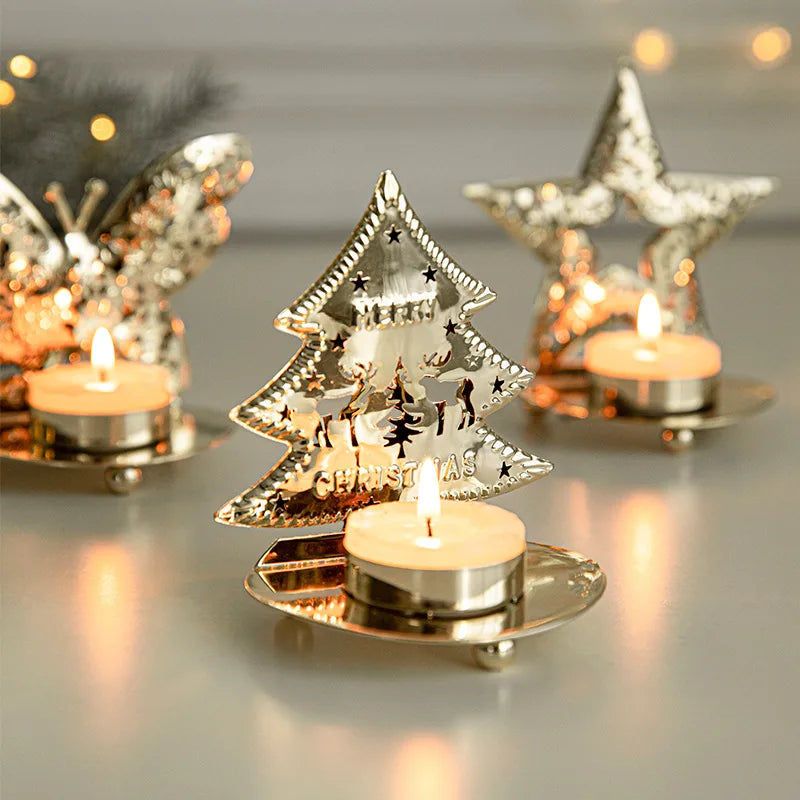 Three lit tea light candles in ornate, shiny metal holders, shaped like a butterfly, a Christmas tree, and a star.