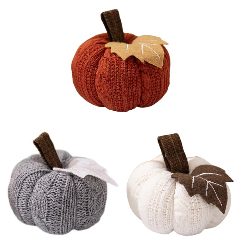 Three knitted pumpkins in orange, gray, and white, each with a brown stem and a fabric leaf, are arranged against a white background.