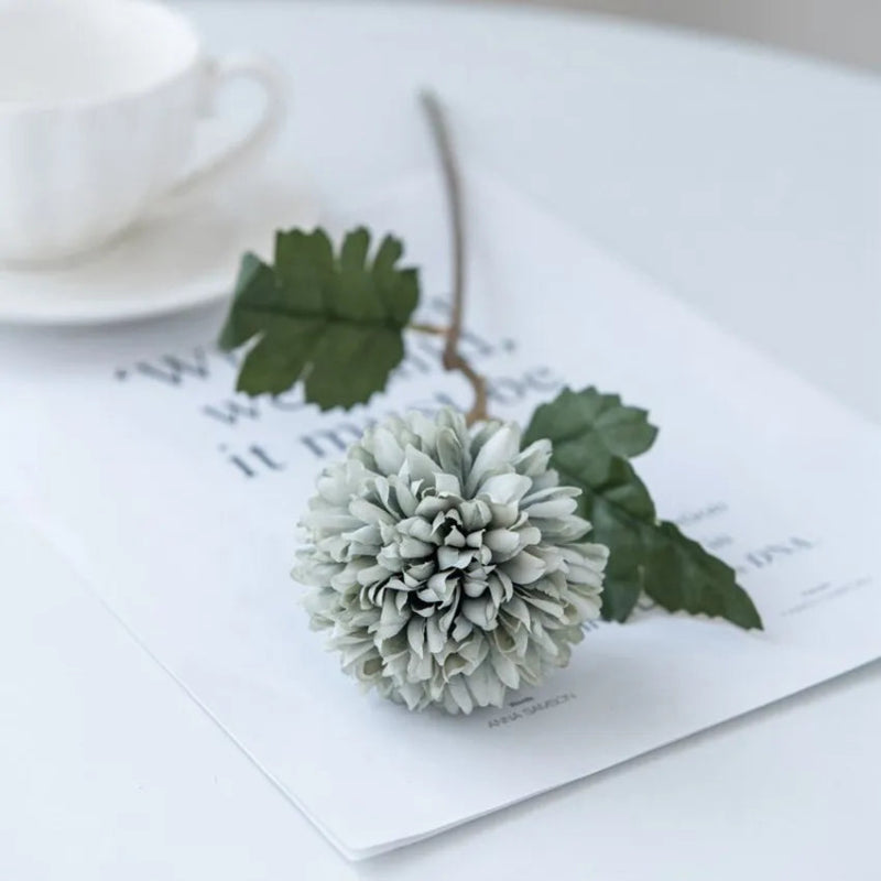 A single gray-green chrysanthemum flower on a white table with a cup.