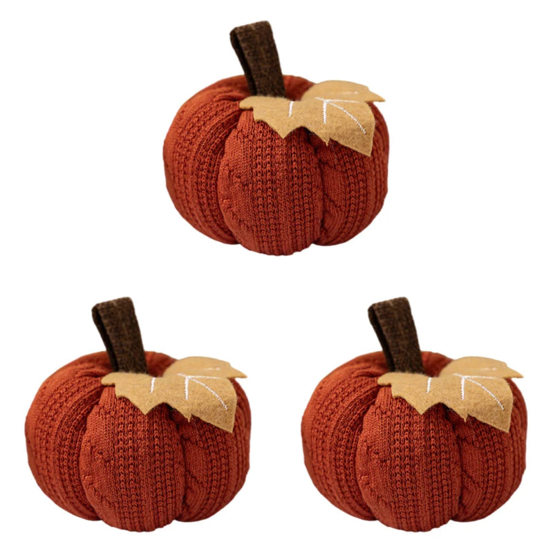 Three identical orange knitted pumpkins, each with a brown stem and a beige felt leaf, are arranged on a white background.