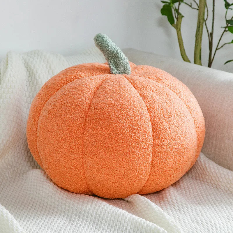 A bright orange, fuzzy, pumpkin-shaped pillow with a light green stem rests on a white textured blanket on a couch.