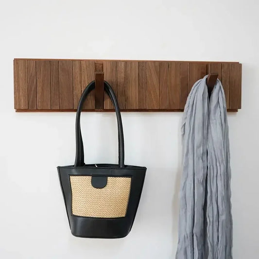 Wooden wall hook holding a black handbag with straw detail and a gray scarf on a white background