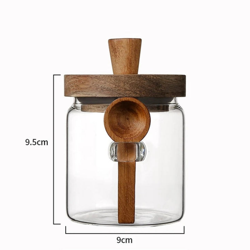 Clear glass jar with wooden lid and spoon, featuring dimensions on a white background.