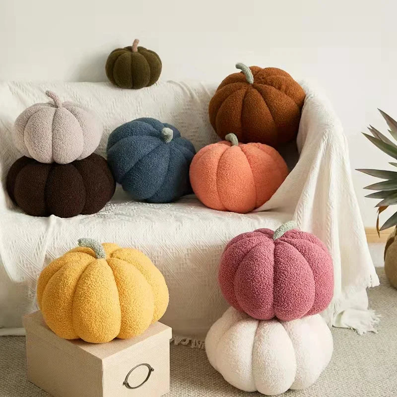 A collection of various sized pumpkin pillows of multiple colors are on a white couch and on the floor.