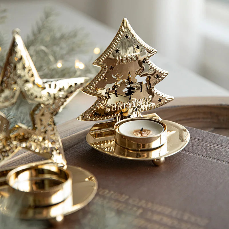 A decorative golden Christmas tree tea light holder with a candle, next to a star-shaped holder without a candle.
