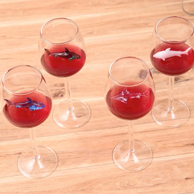 A top-down view of four wine glasses with red wine and small glass shark figurines inside.