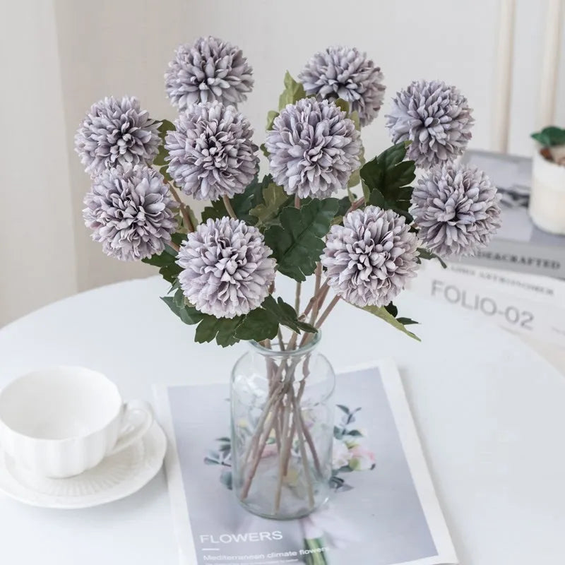 Light purple faux flowers in a clear vase on a white table.