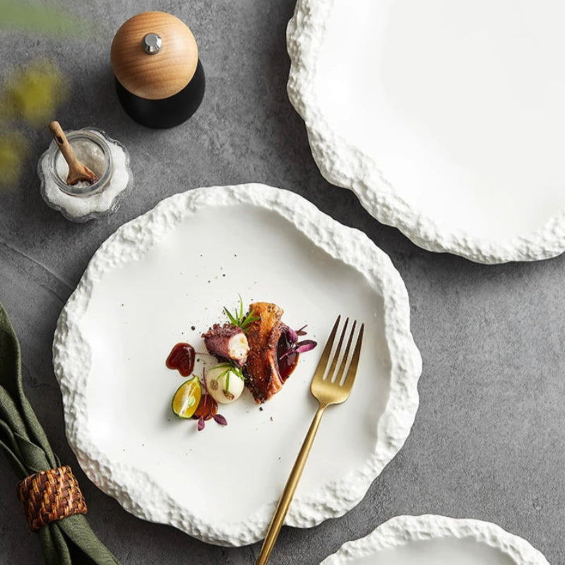 A top-down view of a beautifully plated dish on a textured white plate, accompanied by a golden fork, a salt shaker, and a pepper mill, all resting on a grey surface with a green napkin.