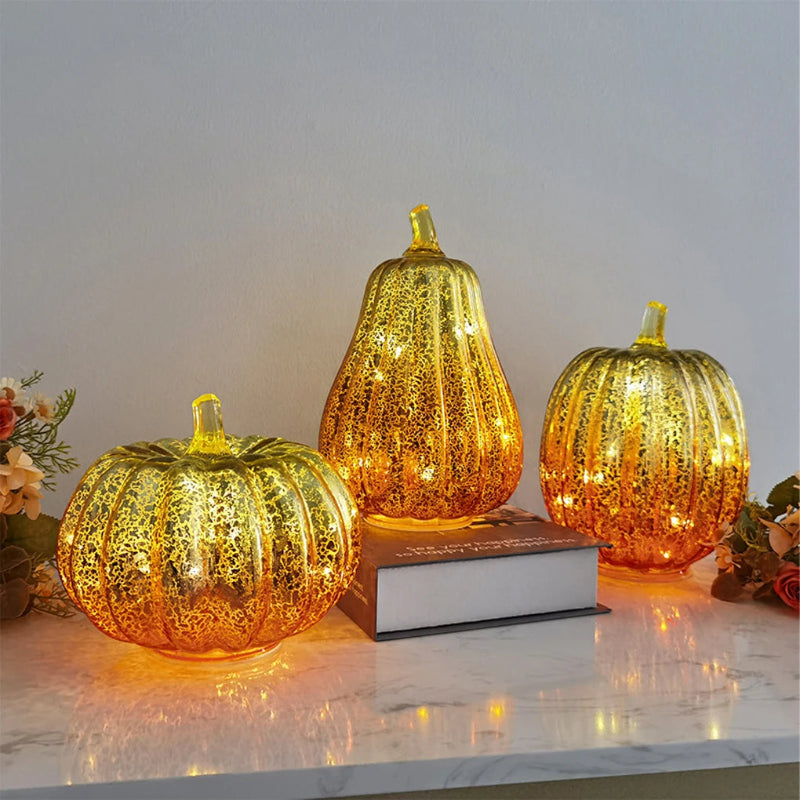 A collection of three decorative, shimmering, gold-colored pumpkins with internal lights sitting on a marble surface.