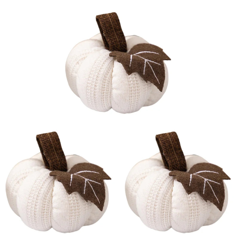 Three identical white knitted pumpkins, each with a brown stem and a brown fabric leaf, are arranged on a white background.