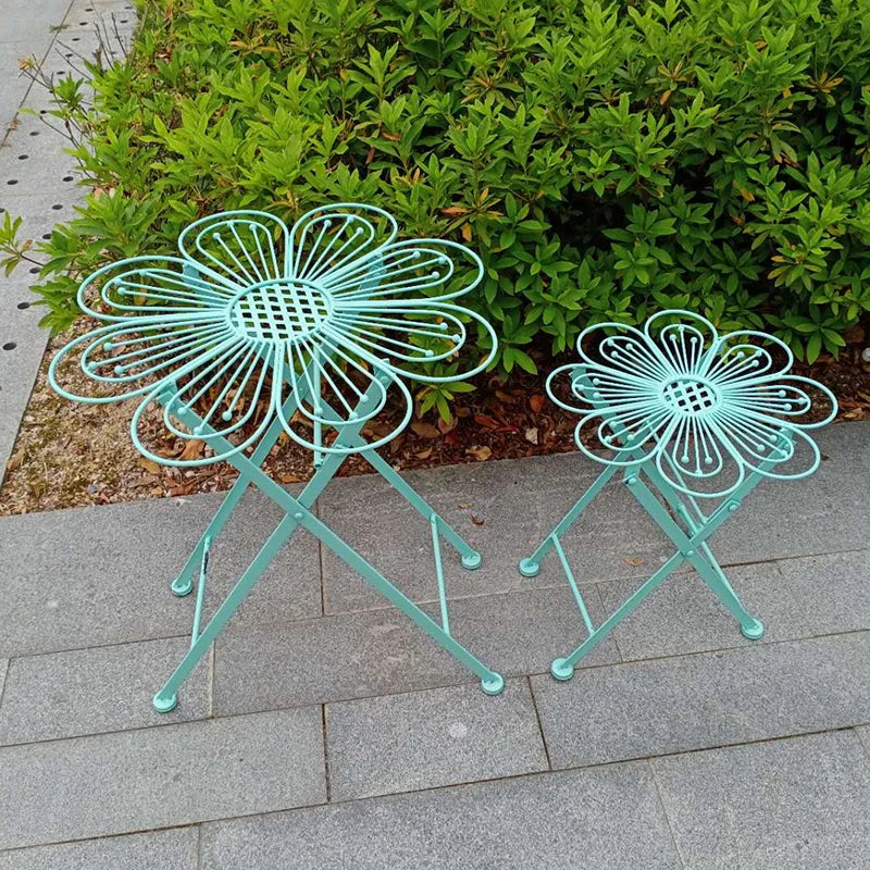 Two turquoise flower-shaped stools on a stone patio with greenery in the background.
