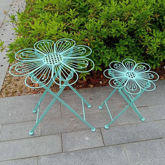 Two turquoise flower-shaped stools on a stone patio with greenery in the background.