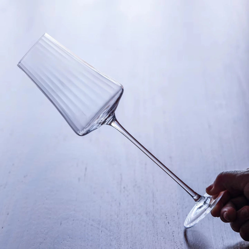A hand holding a clear, fluted wine glass by its base.