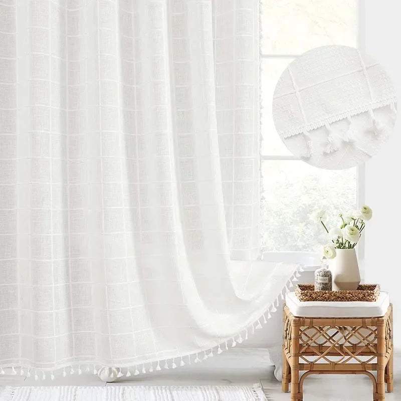 White curtain with tassels in a bright room with a small table and lamp.