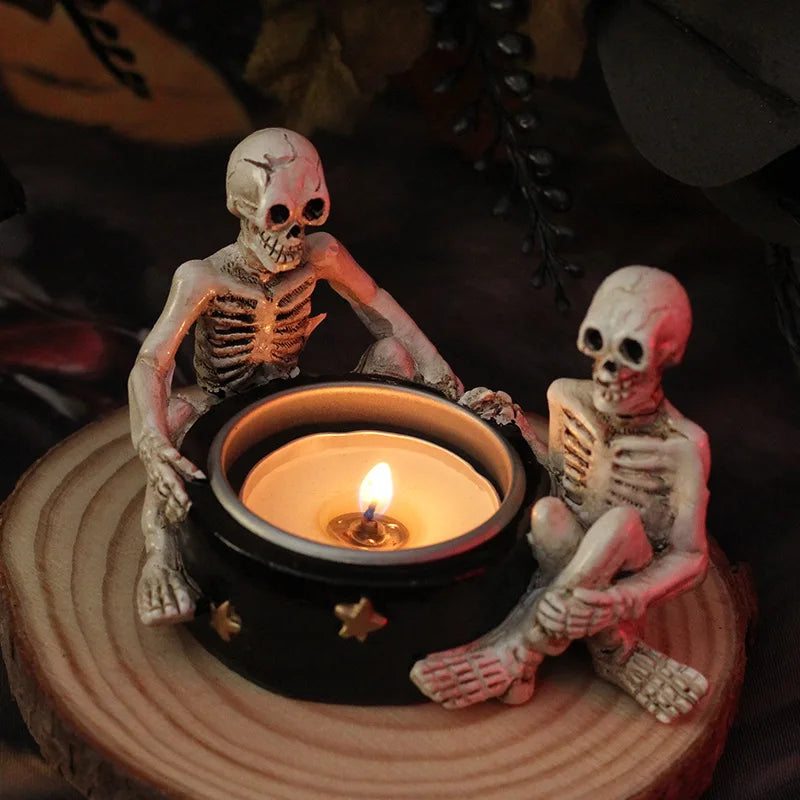 Two skeletons sit on either side of a lit candle, on a wooden surface.