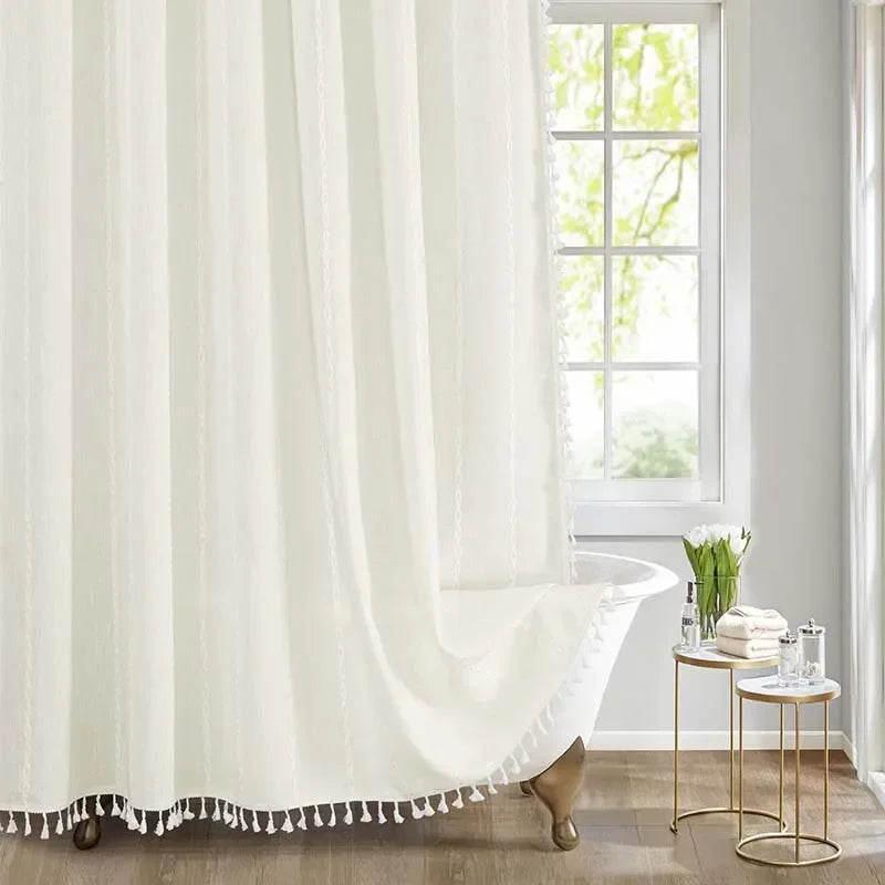 White curtain with tassel trim in a bright room with a window and small table.