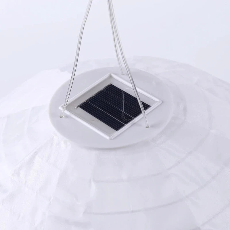 A close-up shot shows the top of a white solar lantern, revealing a square solar panel embedded in a white circular base with hanging wires.