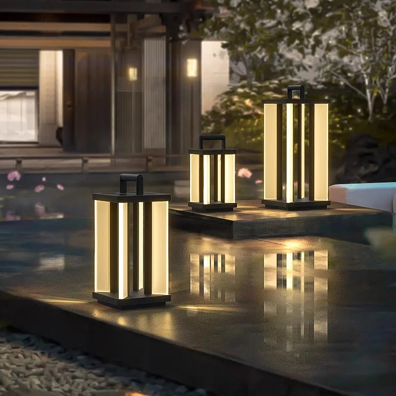 Three illuminated "Villa Solar Lamps" of varying sizes stand on a stone surface next to a reflecting pool at night, with a building and greenery in the blurred background.