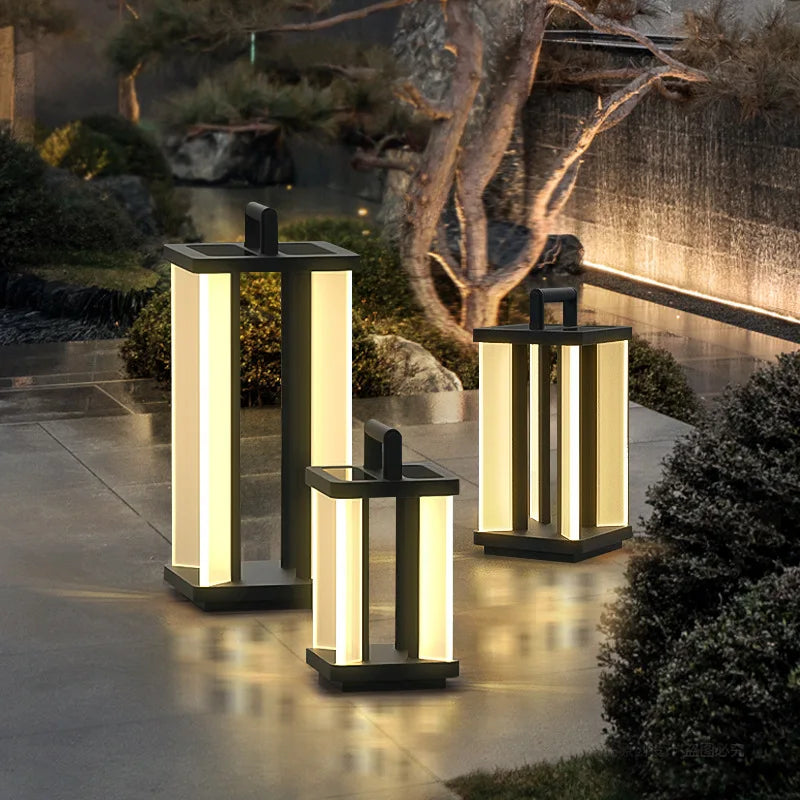 Three illuminated "Villa Solar Lamps" of varying sizes stand on a wet stone surface at night, with lush greenery and a softly lit waterfall feature in the background.