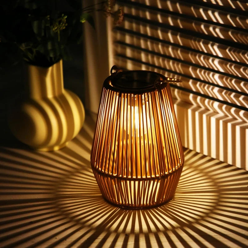 A warm-toned, cylindrical outdoor lantern made of vertical slats casts radiating shadows on a surface near a light-colored vase. The lantern has a dark top, suggesting a solar panel, and a handle for hanging. Light shines through the slats, creating a striped pattern.