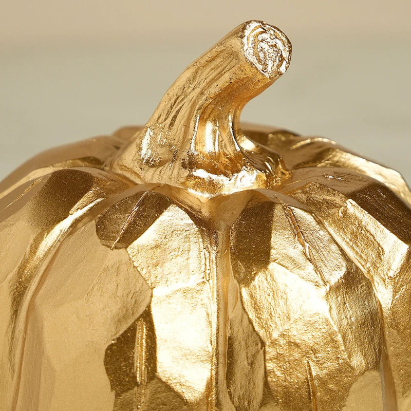 A close-up of a small, decorative golden pumpkin's stem and faceted top.