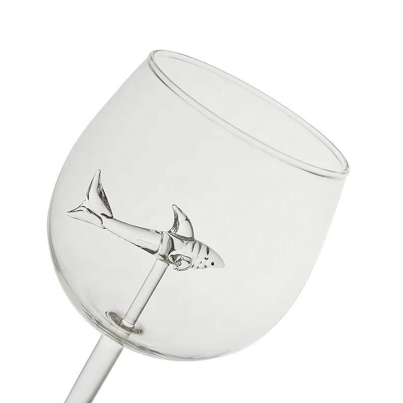 A tilted, empty wine glass with a clear glass shark figurine suspended inside.
