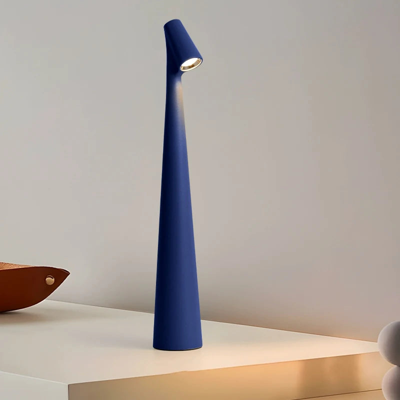 A sleek, modern, blue lamp with a narrow, tall base and a small light at the top, standing on a white surface.