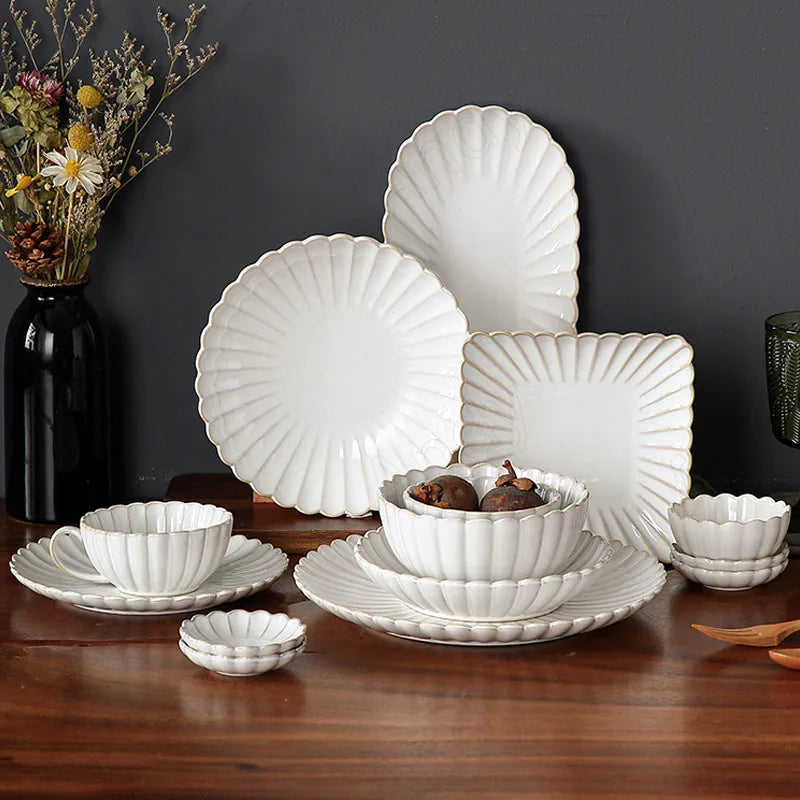 A complete set of white, scalloped-edge ceramic dinnerware with vertical ridges, including various plates, bowls, a cup and saucer, and an oval platter, displayed on a wooden table.