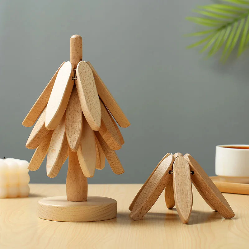 Two light-colored wooden trivets shaped like trees are on a light wooden table. A candle and mug are in the background.