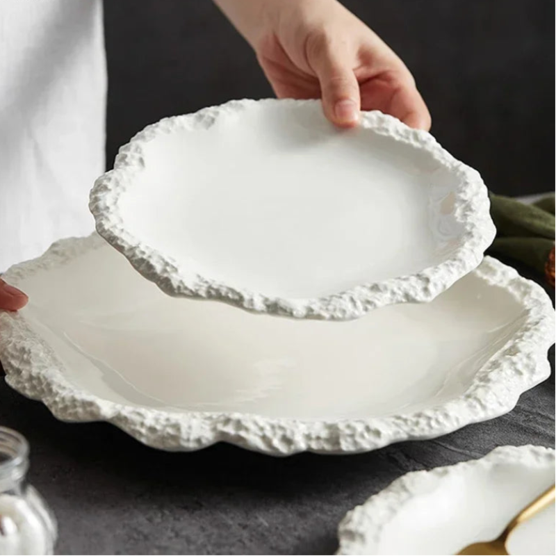 A person's hands placing a white, textured plate on top of another similar plate.