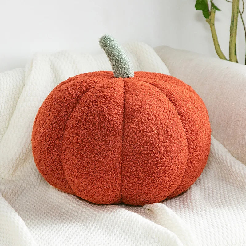 A vibrant orange, fuzzy, pumpkin-shaped pillow with a light green stem rests on a white textured blanket on a couch.