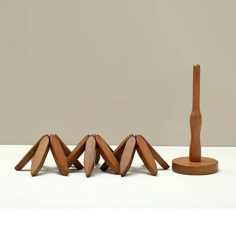 Wooden expandable trivet with a folded zigzag design, placed next to a wooden paper towel holder on a white surface with a beige background.