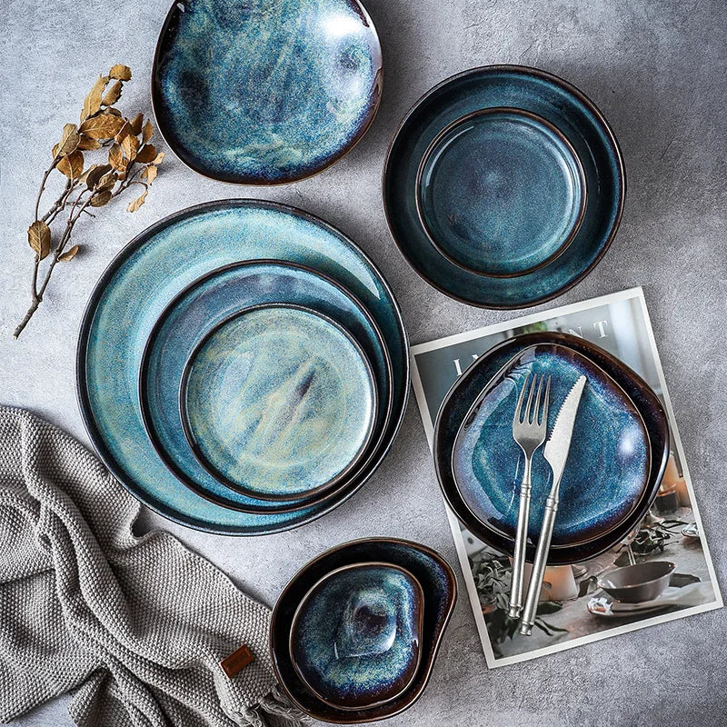 Set of blue ceramic plates and bowls on a gray surface with a magazine underneath.