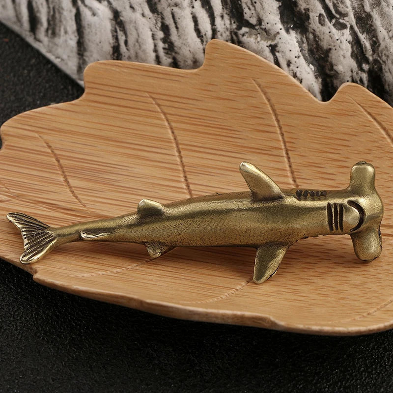 Brass hammerhead shark figurine on a wooden stand with a textured background