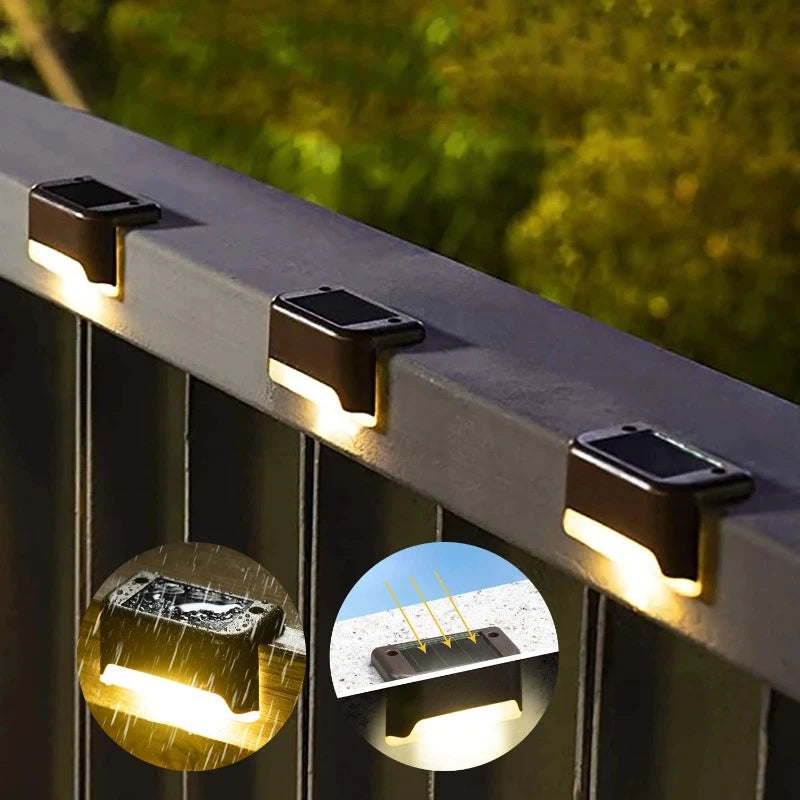 Three small, dark, rectangular solar lights are mounted on a gray railing, casting a warm white downward glow. Insets show a light in the rain and sunlight charging a similar light. Greenery is blurred in the background.