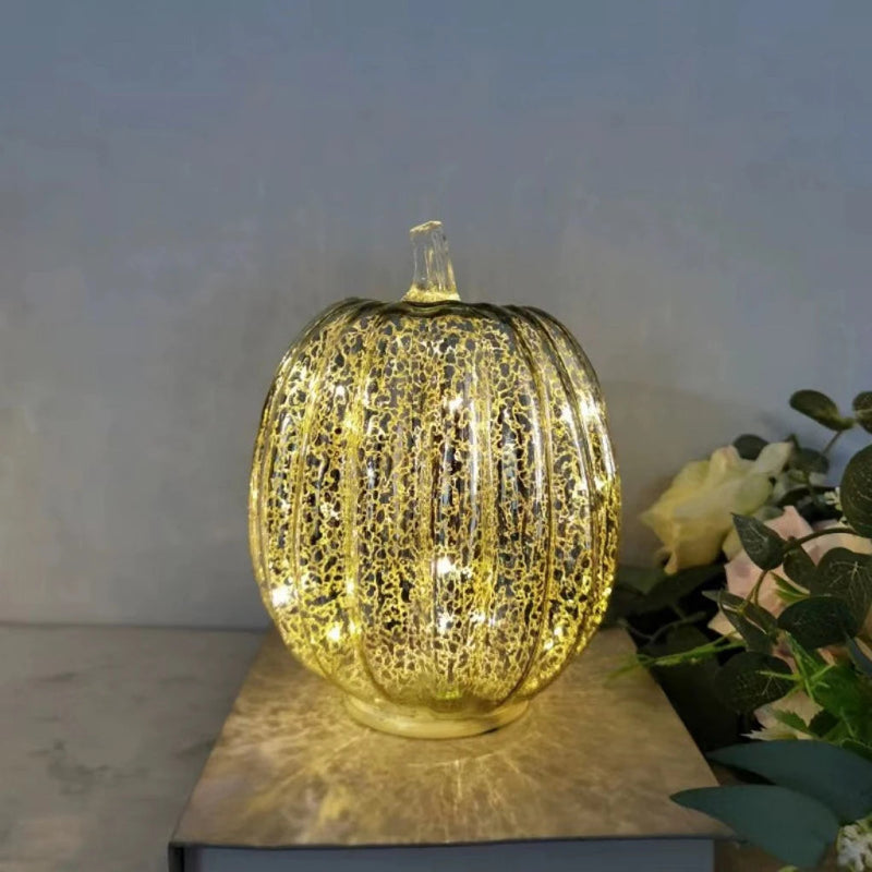 A glowing, round, gold-colored pumpkin decoration with lights inside, sitting on a book.