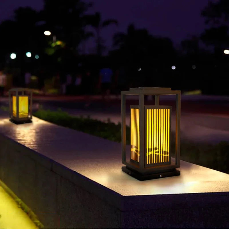 A modern, square, dark-framed outdoor lantern with vertical slats emits a warm glow.