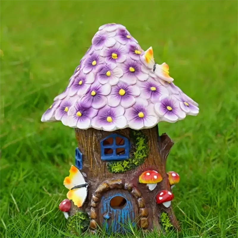 A small fairy house with a purple flower roof, blue door and windows, and mushroom and butterfly decorations sits on green grass.