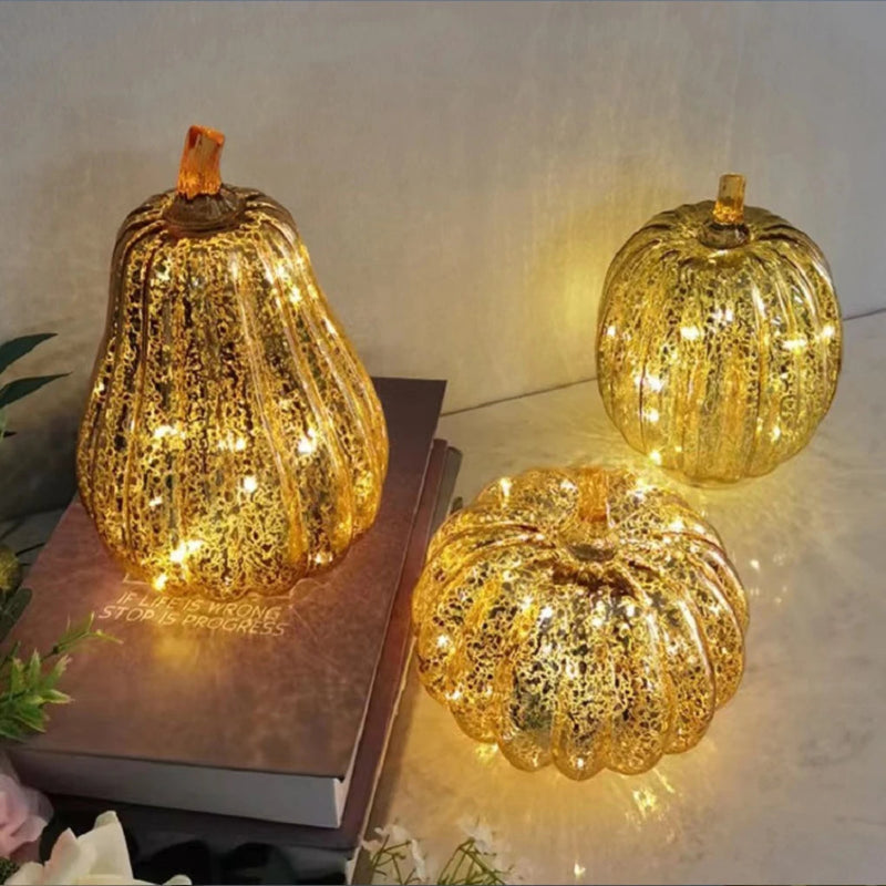 A group of three illuminated, decorative, gold-colored pumpkins with intricate patterns.