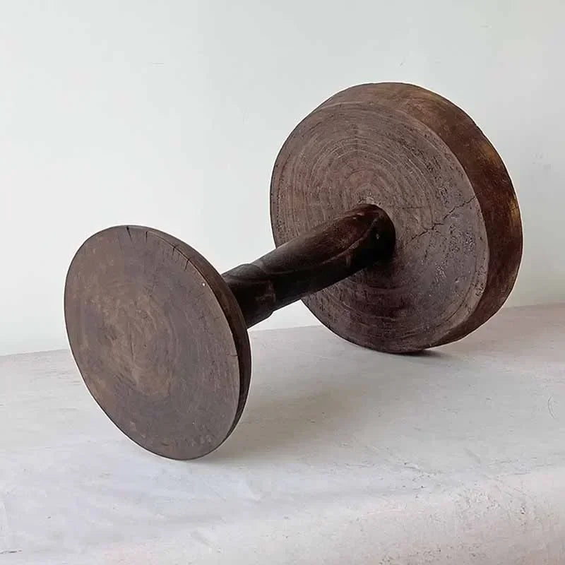 A rustic, dark wood, round side table (Momo Wabi-sabi Log Small Coffee Table) lying on its side, showing its unique shape and texture against a neutral background.