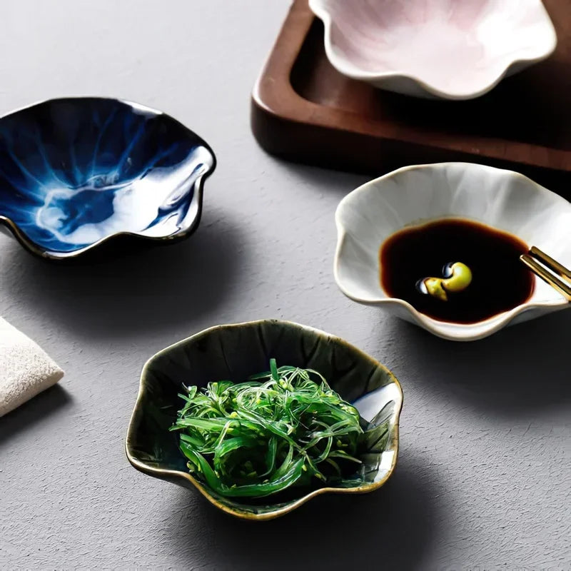 Three small, flower-shaped condiment dishes, one holding seaweed salad and another soy sauce, on a gray surface.